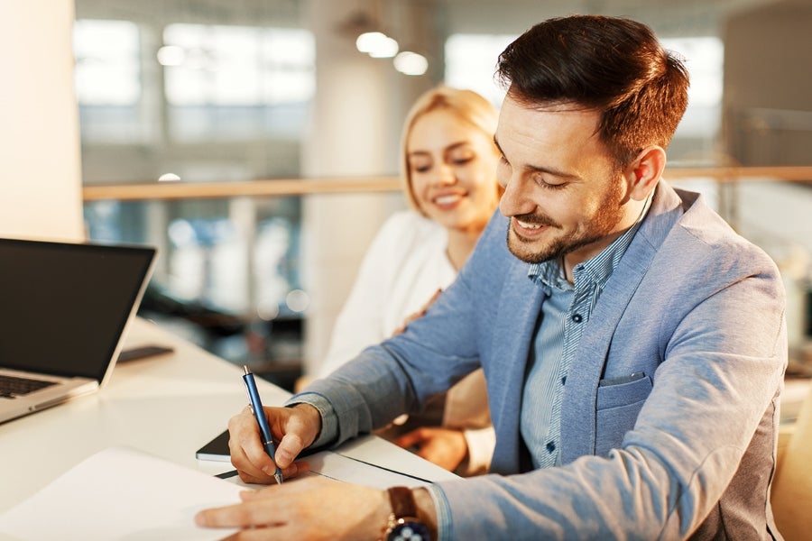 Smiling couple signing documents at a dealership desk