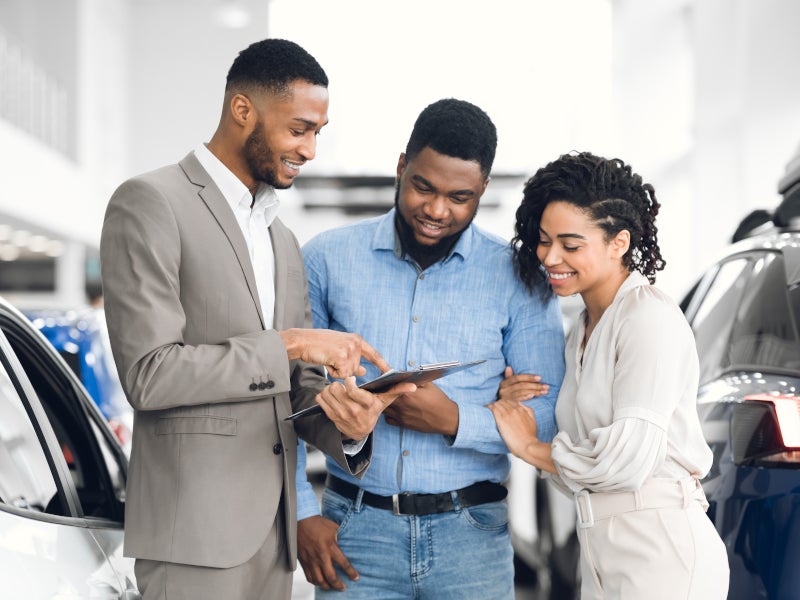 Man handing over car keys to a smiling couple at a dealership