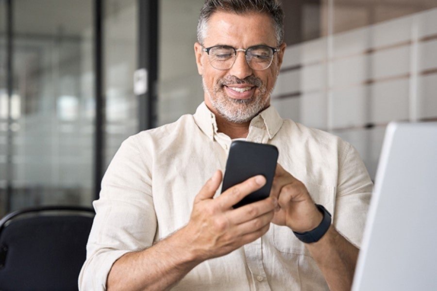 Smiling man using smartphone in front of laptop